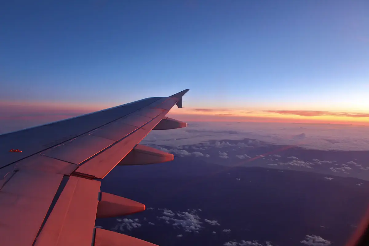 Blick aus dem Flugzeugfenster auf die Tragfläche über den Wolken bei Sonnenuntergang